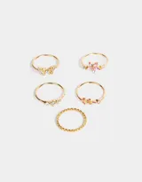 Set de 5 anillos dorados con dijes de flor rosa, mariposa con strass, hojas con strass rosa, strass blancos y un anillo entrelazado.