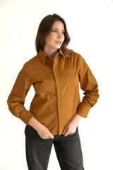 Camisa marrón de corte clásico, con cuello, mangas largas con puños abotonados, cierre frontal con botones al tono, bolsillo de parche en el pecho y ruedo redondeado.