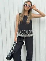 Blusa negra sin mangas con bordado blanco en el ruedo.