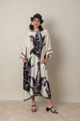 Vestido largo color natural con estampado de hojas de palmera en tonos verdes. Tiene corte amplio tipo túnica, cuello redondo, mangas tres cuartos, bolsillos laterales y ruedo con ribete.