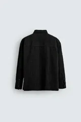 Camisa negra de denim de algodón con textura irregular, corte relaxed fit, cuello solapa, manga larga con puños abotonados y cierre frontal con botones.