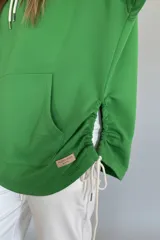 Canguro verde con capucha y cordones blancos, de corte oversize y mangas largas con puños elásticos.