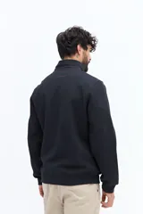 Campera de algodón gris azulado con cierre frontal completo y cuello alto. Presenta detalles de tela técnica azul verdoso en la parte superior del pecho y hombros, y un parche negro con texto blanco en el pecho izquierdo.