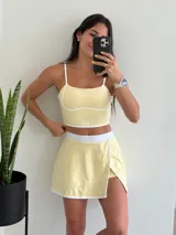 Conjunto deportivo amarillo pálido compuesto por un top con tirantes finos y una minifalda cruzada con short interno.
