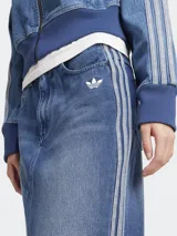 Falda larga de jean azul con corte recto y abertura frontal. Presenta tres tiras blancas verticales a los costados y logo de Adidas bordado en el frente.