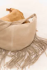 Bolso hobo de cuero gamuza color beige, con flecos largos en el contorno inferior y correa de hombro.