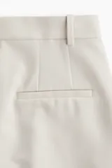 Pantalón de vestir color beige, de corte ancho y tiro alto, con pinzas delanteras, bolsillos laterales y cierre frontal.