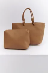 Bolso tipo tote color marrón claro, con textura símil cuero y doble asa de mano con detalle de nudo. Incluye un sobre con cierre.