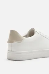 Zapatilla urbana de cuero sintético color negro, con cordones y suela de goma color crema.