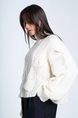 Sweater blanco de punto con cuello alto, diseño de ochos y volados en los hombros.