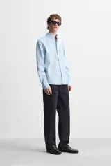 Camisa celeste de corte regular fit, confeccionada en popelín de algodón. Tiene cuello abotonado, manga larga con puños abotonados y cierre frontal con botones.