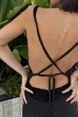 Vestido largo de silueta fluida confeccionado en seda con detalles de encaje. Presenta un diseño negro con estampado de lunares blancos, escote en V profundo y espalda descubierta con tiras cruzadas. La falda cuenta con paneles de encaje que aportan movimiento y delicadeza.