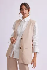 Chaleco largo color beige con solapas, cierre con dos botones y bolsillos delanteros.