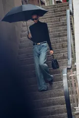 Jersey negro de punto liso con cuello alto, manga larga y detalle de botones dorados en los puños.