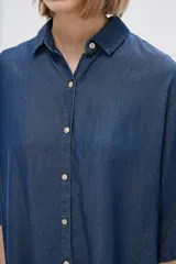 Camisa celeste de manga corta, corte holgado, con cuello camisero y cierre frontal con botones.