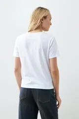 Remera blanca de algodón con cuello redondo y mangas cortas. Presenta un bordado de flores paisley en el hombro izquierdo.