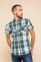 Camisa de manga corta con estampado a cuadros en tonos verde, azul y blanco. Tiene cuello clásico, cierre con botones y dos bolsillos con solapa en el pecho.