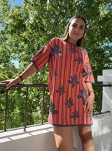 Vestido tejido de algodón con diseño de rayas verticales en tonos beige, marrón y verde azulado, con motivos de hojas grandes en verde azulado. Tiene cuello redondo y manga corta, con un calce holgado.