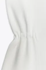 Chaleco blanco de tejido de punto con cuello solapa, sin mangas, detalle de elástico en la cintura y cierre frontal con botones metálicos.