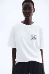 Remera blanca de manga corta con cuello redondo y corte holgado. Presenta un pequeño estampado en el pecho con el texto "LONDON Chelsea Dog Club 1998" y la silueta de un perro salchicha.