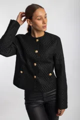 Chaqueta negra con textura, cuello redondo, cierre frontal con botones dorados y bolsillos delanteros con solapa y botón dorado.