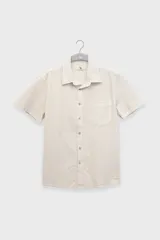 Camisa de manga corta color crema, confeccionada en algodón ligero con textura waffle. Tiene corte cuadrado, bolsillo en el pecho y botones de coco grabados con el logo de Polonio.