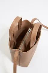 Bolso mini de piel vacuna color negro, con estructura blanda y formato vertical. Tiene doble asa corta, correa larga regulable, cierre con cinta, logo metálico BIMBA Y LOLA, acabados metálicos, bolsillo interior con cierre de cremallera e interior con logo grabado.