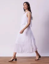 Vestido largo blanco de crepe, con escote redondo y sobrecapa con ruedo de broderie. Corte en la cintura con punto smock.
