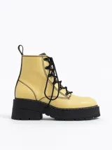 Botín acordonado de cuero color amarillo pastel con pespuntes negros, plataforma track negra y tirador trasero.