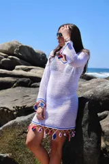 Vestido corto tejido a crochet con hilo de algodón blanco, con mangas largas y cuello en V. Decorado con detalles en azul y rojo, y apliques colgantes con motivos marinos.