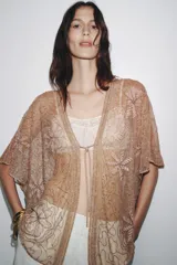 Blusa semitransparente color beige con bordados de hilo metalizado y abalorios. Tiene mangas cortas y cierre frontal con cordones.
