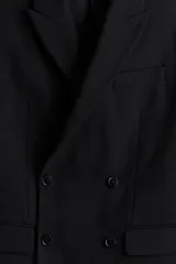 Blazer negro de doble botonadura en tejido suave, con solapas de pico, bolsillo superior, bolsillos ribeteados con solapa adelante y dos bolsillos en el interior. Botones decorativos en los puños y doble abertura atrás. Corte estándar y forro interior.