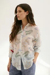 Camisa beige de manga larga con cuello clásico y cierre frontal con botones. Presenta bordados con motivos florales y geométricos en tonos azules, rojos y verdes.