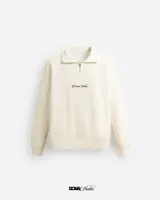 Buzo color crema de corte holgado, con cuello polo y cierre metálico parcial.
