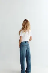 Jeans de tiro medio color azul denim, corte baggy, con trabillas y cinco bolsillos. Cierre frontal asimétrico con cremallera y botones metálicos.