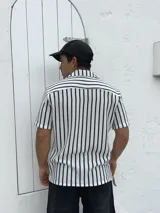 Camisa tejida a rayas verticales blancas y negras, de manga corta y cuello solapa.