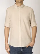 Camisa de manga larga color beige claro, confeccionada en lino y algodón. Tiene cuello abotonado, cierre frontal con botones y bolsillo en el pecho.