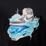 Remera negra de corte recto con estampado de una zapatilla deportiva sobre un fondo de salpicaduras de agua en tonos azules.