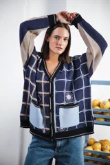 Cardigan oversized de tejido jacquard color crema con diseño de cuadrados en marrón y detalles bordados. Tiene cuello en V, cierre con botones, mangas largas y bolsillos frontales.