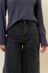 Pantalón de jean negro de pierna ancha y tiro medio-alto, con estampado sutil de leopardo en tono más oscuro y pequeños puntos blancos brillantes.