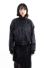 Campera bomber negra de tela satinada con cierre frontal, cuello redondo y puños y cintura elastizados. Tiene un pequeño logo bordado en el pecho y un bolsillo con cierre en la manga. Es reversible.