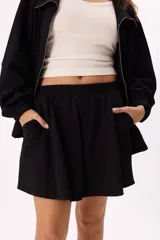 Conjunto deportivo negro compuesto por un buzo con cierre frontal y falda corta. El buzo es de corte holgado, con cuello alto, cierre frontal y mangas largas con puños elásticos. La falda es corta, de corte evasé y cintura elástica.