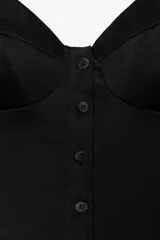 Top negro de popelín con escote pico, tirantes finos ajustables, detalle de pliegues, forro interior combinado y cierre frontal con botones.
