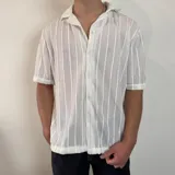 Camisa blanca de crochet con cuello camisero, manga corta y cierre frontal con botones.