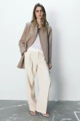 Abrigo color beige confeccionado en lana. Tiene cuello subido, mangas largas con hombreras, forro interior combinado y cierre frontal cruzado con botones metálicos.