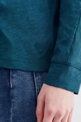 Remera blanca de algodón con calce relajado y cuello redondo. Tiene mangas largas que se ajustan hacia los puños.