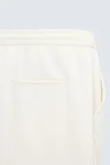 Bermuda color crudo de corte recto, con cintura elástica ajustable con cordón, pliegues frontales, bolsillos laterales y bolsillos traseros de vivo.