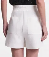 Short de vestir blanco de corte sastrero, con cintura alta, bolsillos laterales y detalle de hebilla metálica plateada en la cintura.