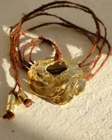 Collar con cordón naranja y dije de flor dorada.