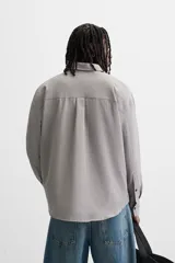 Camisa de hombre relaxed fit con cuello solapa, manga larga con puño abotonado, bolsillo de parche en el pecho y cierre frontal con botones. Diseño a cuadros en tonos gris y blanco.